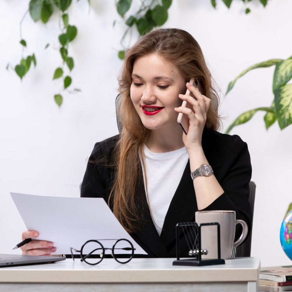 front-view-young-beautiful-lady-white-shirt-black-jacket-using-her-laptop-front-table-smiling-talking-phone-working-with-documents